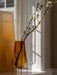 Echasse Vase in amber glass with a black stand, holding a flowering branch, bathed in sunlight on a windowsill.
