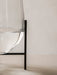 A close-up of the clear glass Echasse Vase, filled with water and cradled in its black metal stand against a neutral wall.