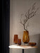 A collection of amber glass Echasse Vases and an Echasse Bowl by Audo CPH, styled on a light marble table with a branch.