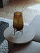 A small Hasse Vase in amber glass with dried grasses, placed on a light marble Androgyne Side Table next to a textured sofa.
