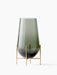 Echasse Vase M, a teardrop-shaped, smoked green glass vase on a slender, minimalist four-legged brass stand.