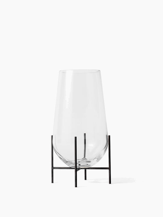 The small Echasse Vase in clear glass shown from the front. The teardrop-shaped vase sits in a minimal black metal stand.