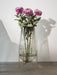 The large Echasse Vase in smoked glass on a brass stand, holding three pink chrysanthemums, on a grey surface.