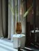A large amber glass Hasse Vase with tall foxtail lilies sits on a white Androgyne Side Table in a sunlit room by curtains.