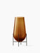 A small Hasse Vase in translucent amber glass, presented in a minimalist bronze-brass stand against a plain white background.