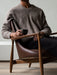 A person wearing a brown jumper sits in the Elizabeth Lounge Chair, which has a dark walnut frame and brown leather.