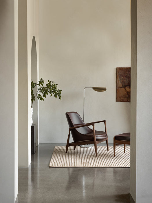 A living room featuring the brown leather Elizabeth Lounge Chair, matching Ottoman, and a Wing Floor Lamp on a striped rug.
