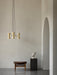 A brown leather Elizabeth Ottoman and a black marble Plinth Tall sit under a Collector Chandelier in a minimalist room.