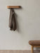 A brown jacket hangs from a wall-mounted wooden Epoch Rack. Below, a brown Brasilia Ottoman sits on a textured Houkime Rug.