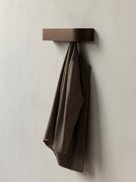 A minimalist dark oak Epoch Rack mounted on a light-coloured wall, with a brown textured blazer jacket hanging from it.