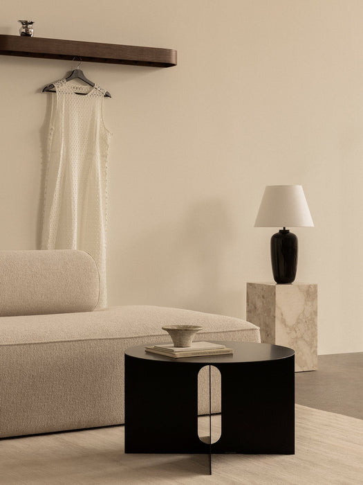 A beige Eave Sofa and black Androgyne Table. A Torso Lamp sits on a marble Plinth, with an Epoch Shelf on the wall behind.