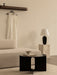 A beige Eave Sofa and black Androgyne Table. A Torso Lamp sits on a marble Plinth, with an Epoch Shelf on the wall behind.