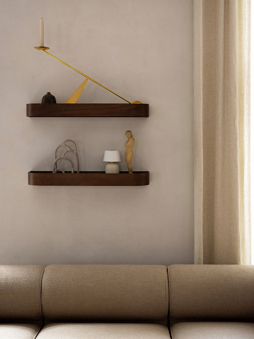 Two dark wood floating shelves mounted on a beige wall, styled with a modern brass candle holder and sculptures.