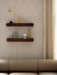 Two dark wood floating shelves mounted on a beige wall, styled with a modern brass candle holder and sculptures.