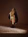 Flambeau Candle Holder sits on a rustic wooden table, its brass reflector catching the light from a single, smoking candle.
