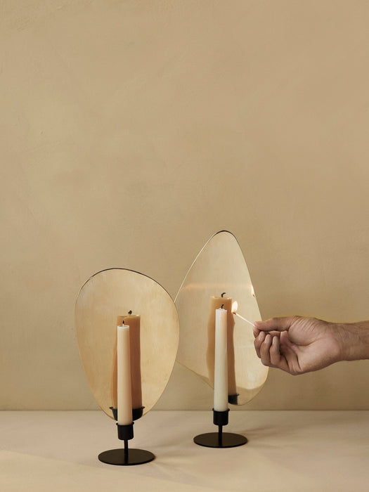 A hand lights a candle in a black Flambeau Candle Holder with a brass reflector. An identical holder sits beside it.