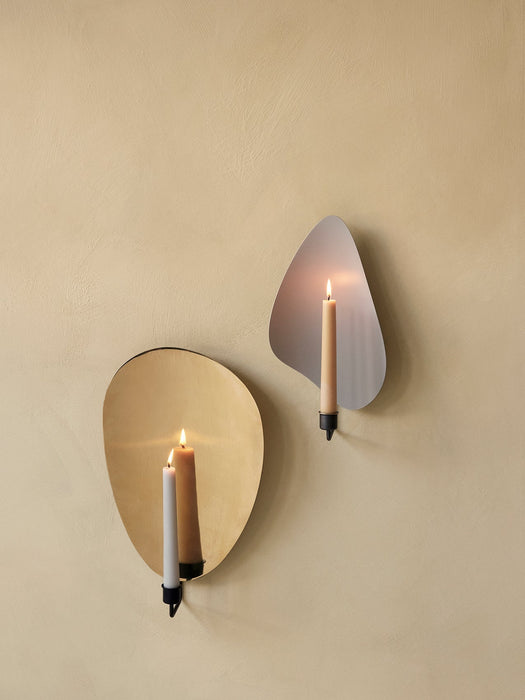 Two Flambeau Wall Candle Holders, brass and steel, mounted on a textured beige wall with lit candles casting a warm glow.