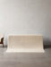 The ivory Gravel Rug draped over a plinth, showcasing its knobbly wool texture in a minimalist room with a concrete floor.
