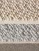A detailed close-up of the Gravel Rug, showing the soft, pebbled wool texture in ivory and light grey on a concrete floor.