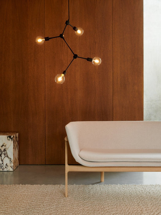 Side view of a Tailor Sofa on a Gravel Rug, with a Franklin Chandelier and marble Plinth against a dark wood wall.
