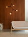 Side view of a Tailor Sofa on a Gravel Rug, with a Franklin Chandelier and marble Plinth against a dark wood wall.