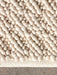 A close-up shot of the Gravel Rug in ivory, showing its bumpy, pebble-like wool texture against a grey concrete floor.