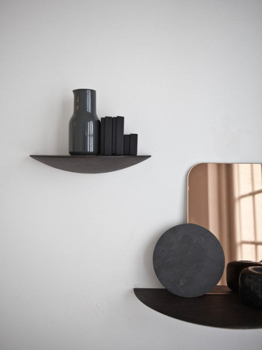 On a white wall, two dark wood Gridy Fungi Shelves. The top holds a grey vase and books, the bottom a stone disc and mirror.