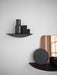 On a white wall, two dark wood Gridy Fungi Shelves. The top holds a grey vase and books, the bottom a stone disc and mirror.