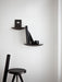 A minimalist room with two dark Gridy Fungi Shelves mounted on a white wall, styled with black books, next to a black stool.