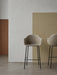 Two beige upholstered Harbour Bar Chairs with black steel frames stand in a minimalist room with colour-blocked walls.