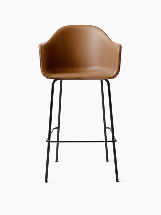 A front view of the Harbour Bar Chair, Upholstered, with a tan leather seat and a slender black metal base with a footrest.