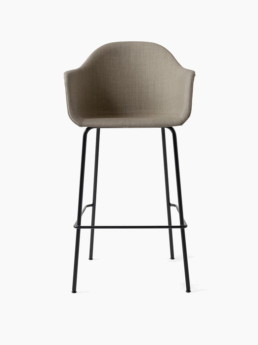 Front view of the Harbour Bar Chair, Upholstered, with a light brown fabric seat and slender black steel legs with footrest.
