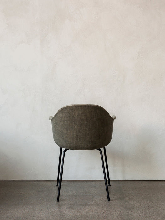 Back view of the Harbour Dining Chair, with dark textured upholstery and a black steel base, against a textured white wall.