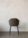 Back view of the Harbour Dining Chair, with dark textured upholstery and a black steel base, against a textured white wall.