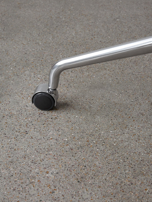Close-up of a Harbour Dining Chair's polished aluminium star base with a black caster wheel on a grey floor.