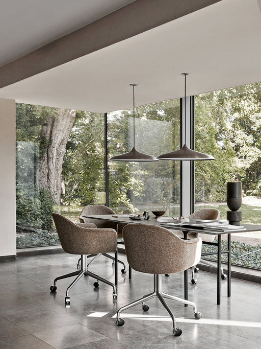 Four brown upholstered Harbour Dining Chairs with polished star bases and casters around a table by a large window.