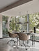Four brown upholstered Harbour Dining Chairs with polished star bases and casters around a table by a large window.