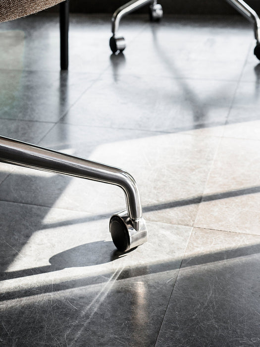 Harbour Dining Chair showing a close-up of its polished aluminium star base and caster wheel on a sunlit grey tiled floor.