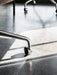 Harbour Dining Chair showing a close-up of its polished aluminium star base and caster wheel on a sunlit grey tiled floor.