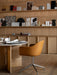 A tan Harbour Dining Chair at a marble-topped Androgyne Dining Table in a studio with wooden shelves of material samples.