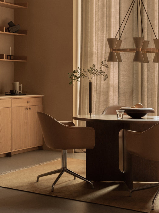 A warmly lit dining room featuring brown Harbour Dining Chairs with polished star bases pulled up to a dark Androgyne Table.