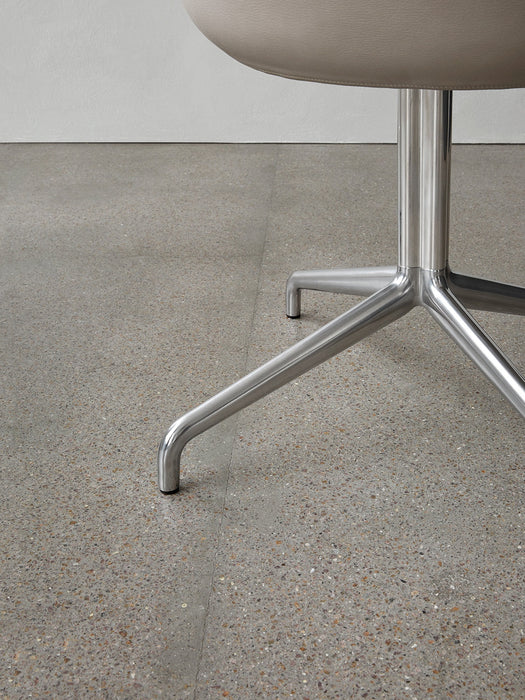 A close-up of the Harbour Dining Chair's polished aluminium star base, with its four legs on a grey terrazzo floor.