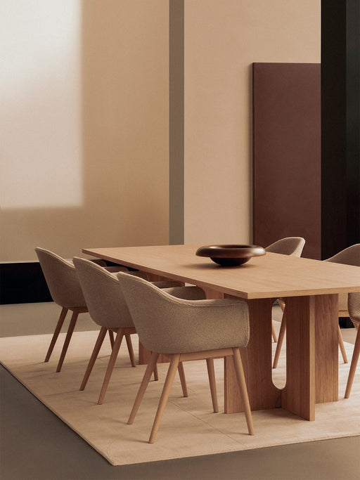 A light oak Androgyne Dining Table with beige Harbour Dining Chairs on a rug. A dark Releve Platter sits on the table.