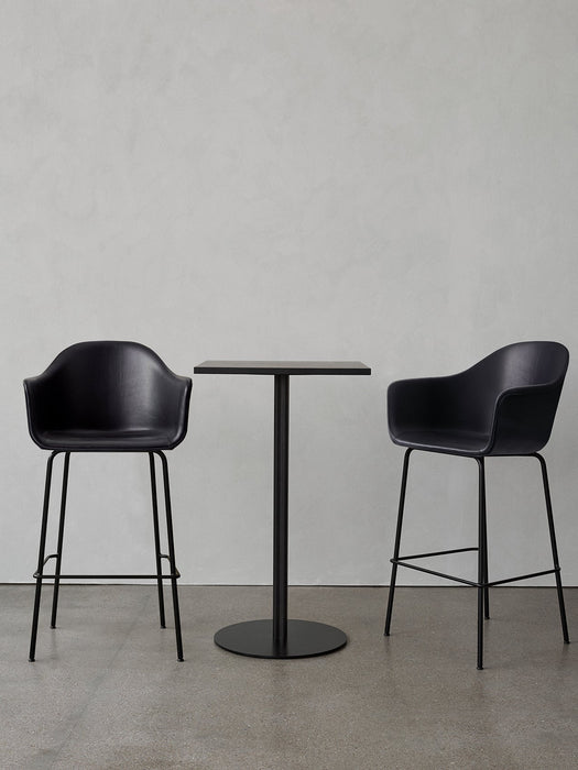 A black Harbour Column Bar Table with a rectangular top and round base, flanked by two black upholstered Harbour Bar Chairs.