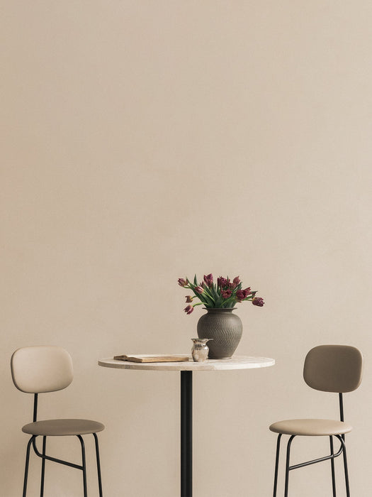 A Harbour Column Bar Table with a marble top, flanked by two beige Afteroom Bar Chairs. A vase of tulips decorates the table.