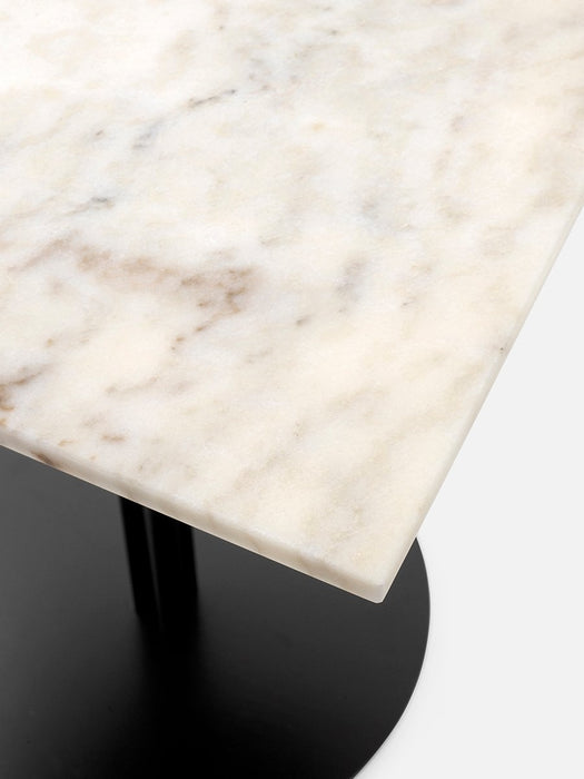 A close-up view of the corner of a Harbour Column Table, showing the off-white marble tabletop and black column base.