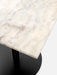 A close-up view of the corner of a Harbour Column Table, showing the off-white marble tabletop and black column base.