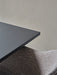 A close-up view showing the corner of the charcoal Harbour Column Table and the textured upholstery of a Harbour Chair.