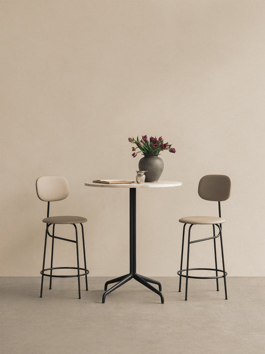 A marble-top Harbour Column Counter Table with a black star base, a vase of tulips and two Afteroom Counter Chairs.