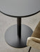 A high-angle close-up of the black Harbour Column Dining Table and olive velvet Harbour Chair on a grey concrete floor.